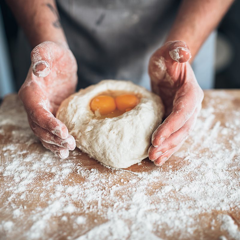 Male baker hands mix the dough with egg. Bread preparation. Homemade bakery